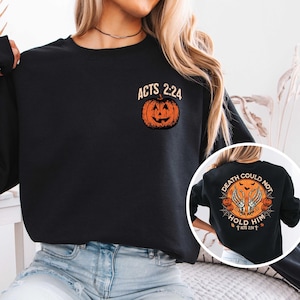 May include: Black sweatshirt with a small orange pumpkin graphic and the text "ACTS 2:24". A circular graphic on the back features a skeleton hand design, pumpkins, and the text "DEATH COULD NOT HOLD HIM ACTS 2:24".