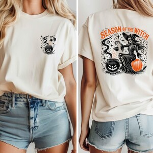 以下が含まれることがあります： ハロウィーンをテーマにしたグラフィックのクリーム色のTシャツ。前面には、不気味な顔と蒸気のある大釜が描かれています。背面には、カボチャを持ったスケルトンの魔女と、オレンジ色のテキスト「SEASON OF THE WITCH」が表示されています。