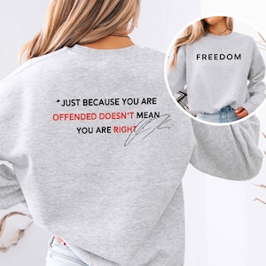 May include: A light gray sweatshirt with the word "FREEDOM" printed in black on the front. The back of the sweatshirt features the quote "JUST BECAUSE YOU ARE OFFENDED DOESN'T MEAN YOU ARE RIGHT" in black and red.