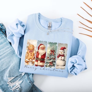 Puede incluir: Sudadera azul claro con un dise&ntilde;o navide&ntilde;o. El gr&aacute;fico incluye un hombre de jengibre, Pap&aacute; Noel, un &aacute;rbol de Navidad y un mu&ntilde;eco de nieve. Las palabras "Merry Christmas" est&aacute;n escritas debajo. La sudadera se muestra con unos vaqueros azules.