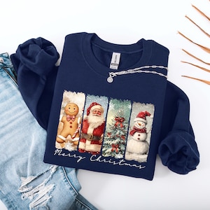 Puede incluir: Sudadera azul marino con un dise&ntilde;o navide&ntilde;o. El gr&aacute;fico presenta un hombre de jengibre, Pap&aacute; Noel, un &aacute;rbol de Navidad y un mu&ntilde;eco de nieve. Las palabras "Merry Christmas" est&aacute;n escritas debajo. Un collar plateado con un colgante est&aacute; en la sudadera.