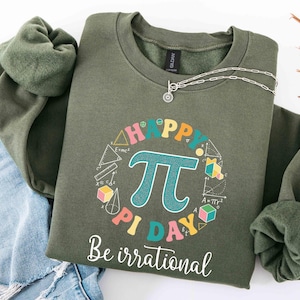 May include: An olive green sweatshirt with the words "HAPPY PI DAY" and the pi symbol in a colorful design. The phrase "Be irrational" is printed below. A silver necklace with a sun-shaped pendant is on the sweatshirt.