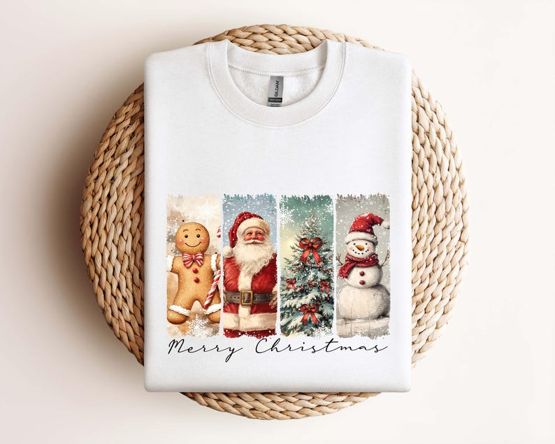 Puede incluir: Sudadera blanca con un dise&ntilde;o festivo de acuarela. Presenta un hombre de jengibre, Pap&aacute; Noel, un &aacute;rbol de Navidad y un mu&ntilde;eco de nieve, con "Merry Christmas" escrito debajo. La sudadera se muestra sobre una superficie circular tejida.