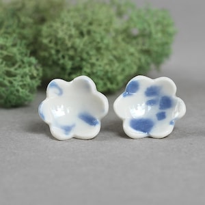 Puede incluir: Un par de pendientes de cerámica con forma de flor, con base blanca y diseños pintados en azul.