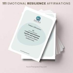 May include: A pile of affirmation cards, featuring the text "111 EMOTIONAL RESILIENCE AFFIRMATIONS." The cards have a light blue and white design with the Azura Therapies logo. One card reads "Today's Affirmation: I create space between reaction and response."