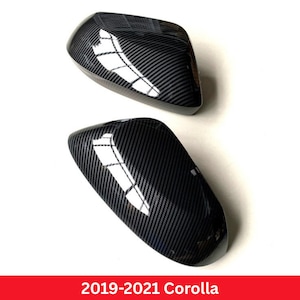 May include: Two black carbon fiber pattern side mirror covers for a 2019-2021 Corolla. These automotive exterior accessories feature a glossy finish with a diagonal weave texture and a curved, aerodynamic shape designed for vehicle side mirrors.