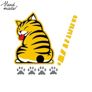May include: A yellow cartoon cat with black stripes, a red tongue, and a smiling expression. The cat is sitting down with paw prints below and a yellow striped design to the right. The words "Hand made" are in the upper left corner.