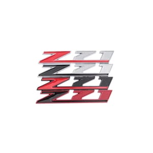 Può includere: Diversi emblemi Z71 rossi, neri e argentati, disposti a pila. Gli emblemi presentano un design stilizzato "Z" e "71". Le parole "hand made" sono visibili nell'angolo in alto a sinistra.