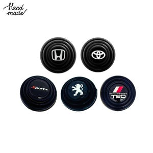 May include: A collection of five black car door protectors with various logos, including Honda, Toyota, Peugeot, and TRD. The text "Hand made" is in the upper left corner. These are likely automotive accessories.