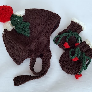 May include: A brown knitted hat and matching mittens with a white and red pom-pom, green holly leaves, and red berries. The hat has a long tie.