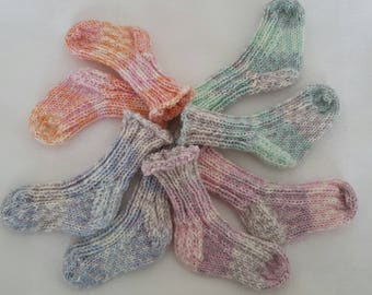 May include: A collection of six small, hand-knitted socks arranged in a circular pattern. Each sock features a unique variegated yarn colorway, including shades of orange, pink, blue, green, and purple, all crafted with a ribbed cuff.