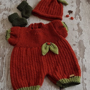 May include: A knitted pumpkin-themed baby outfit in orange and green. The outfit includes a hat, a one-piece jumpsuit, and booties.