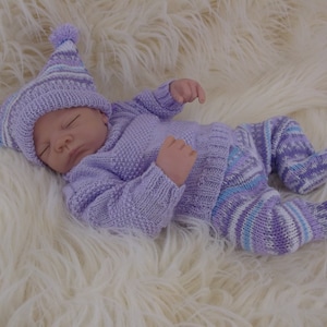 May include: A purple knitted baby outfit with a matching hat. The hat has a white pom-pom on top. The outfit is made of soft, cozy yarn.