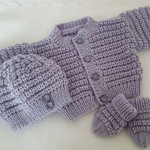 Puede incluir: Un conjunto de punto de beb&eacute; de color lavanda con gorro y botines a juego. El conjunto presenta un cierre de bot&oacute;n y un patr&oacute;n de punto texturizado.