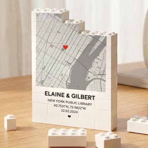 May include: A white block-style decorative item featuring a map of New York City with a red heart marker. The text "ELAINE & GILBERT" and other details are printed below the map. Additional white blocks are scattered around.
