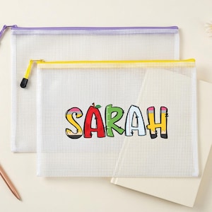 May include: Two clear mesh zipper pouches, one with a purple zipper and the other with a yellow zipper. The front pouch has the name "SARAH" in colorful block letters. A rose gold pen and a notepad are also in the image.