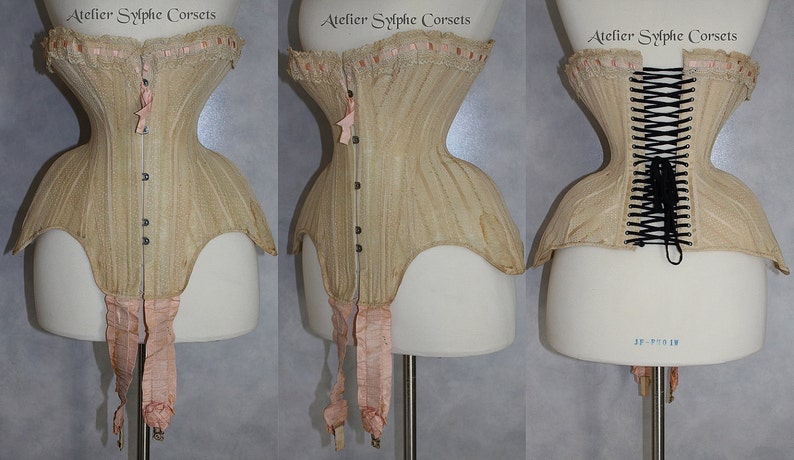 May include: A beige corset with a lace trim and pink ribbon accents. The corset is laced up the back with black laces. The corset is on a white mannequin.