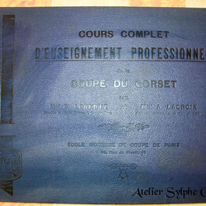 Puede incluir: Un libro azul titulado "COURS COMPLET D'ENSEIGNEMENT PROFESSIONNEL COUPE DU CORSET" de MEZ JORENTZIA & ML LACROIX. El libro es de la ECOLE MODERNE DE COUPE DE PARIS y presenta el logotipo de Atelier Sylphe Corsets.