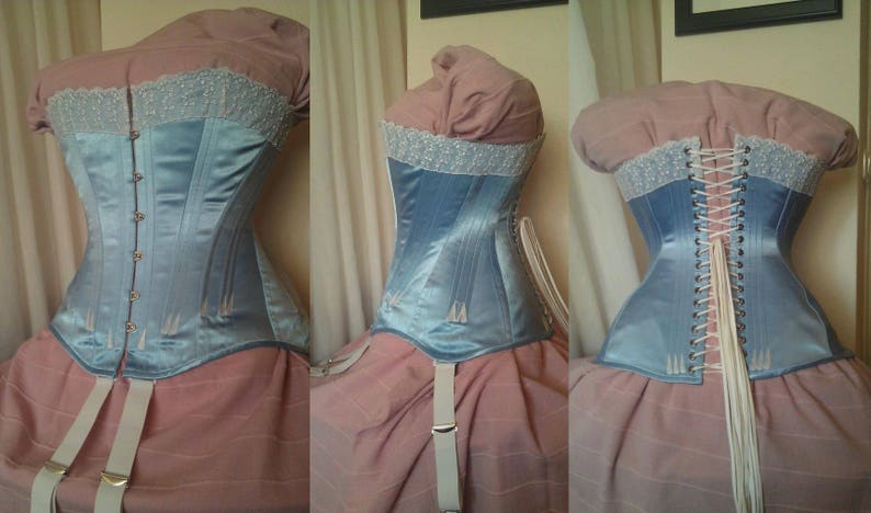 May include: A light blue satin corset with white lace trim and a back lacing system. The corset is shown on a dress form with a pink skirt.