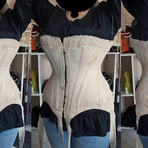 May include: A white cotton corset with lace trim and a front closure. The corset has a boned structure and is shown being worn by a person.