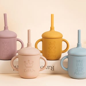 K&ouml;nnte beinhalten: Vier Babybecher aus Silikon mit Deckeln und Strohhalmen in ged&auml;mpften Farben: Mauve, Pfirsich, Senfgelb und Blau. Jeder Becher hat ein anderes Tierdesign und einen Namen. Die Becher haben Griffe.