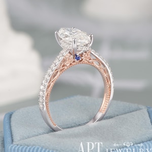 May include: A marquise-cut solitaire ring featuring a white center stone set in silver-toned metal. The band is accented with rose gold leaf-shaped details, small clear stones along the shank, and a single small blue stone at the base of the setting.