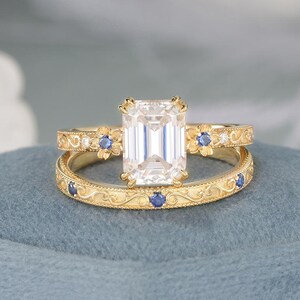 Conjunto de anillo de compromiso Art Déco con moissanita talla esmeralda, banda con detalles de zafiro vintage y detalles de filigrana, diseño floral inspirado en la naturaleza.