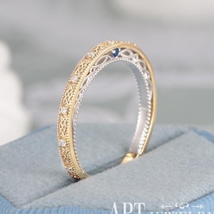 May include: A two-tone ring featuring a yellow gold outer band with an intricate filigree pattern and small embedded clear stones, contrasted by a silver-toned inner band. A single small blue stone is set at the top of the ring band.