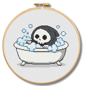 May include: A cross-stitch embroidery hoop featuring a pixelated image of a cartoon Grim Reaper character in a bathtub filled with bubbles. The Grim Reaper has a skull face and is wearing a black hood. The bathtub is white with small feet.