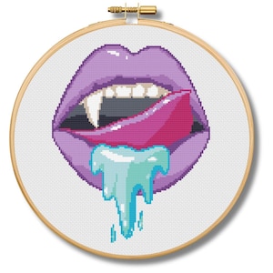 May include: Cross-stitch embroidery of a mouth with purple lips, a pink tongue, and a blue liquid dripping from the mouth. The mouth has two fangs and is set in a wooden embroidery hoop.