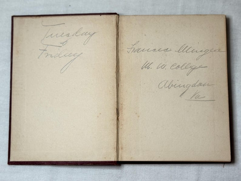 May include: An open vintage book with handwritten text. The left page has "Tuesday" and "Friday" written in cursive. The right page has a name, college, and location written in cursive.