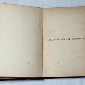 May include: An open book with cream-coloured pages. The right-hand page features the text "SELECT ESSAYS AND ADDRESSES" in black. The book has a dark red-brown binding. The pages show signs of age and use.