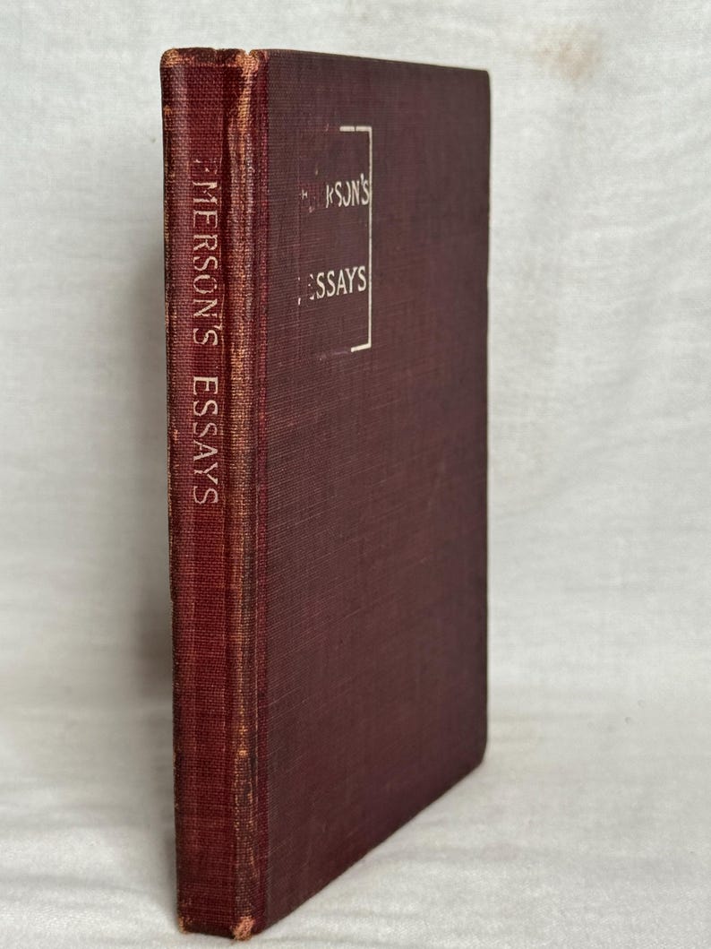 May include: A maroon-coloured hardcover book titled "Emerson's Essays." The spine displays the title vertically, while the front cover features the title within a white rectangular frame. The book has a worn appearance.