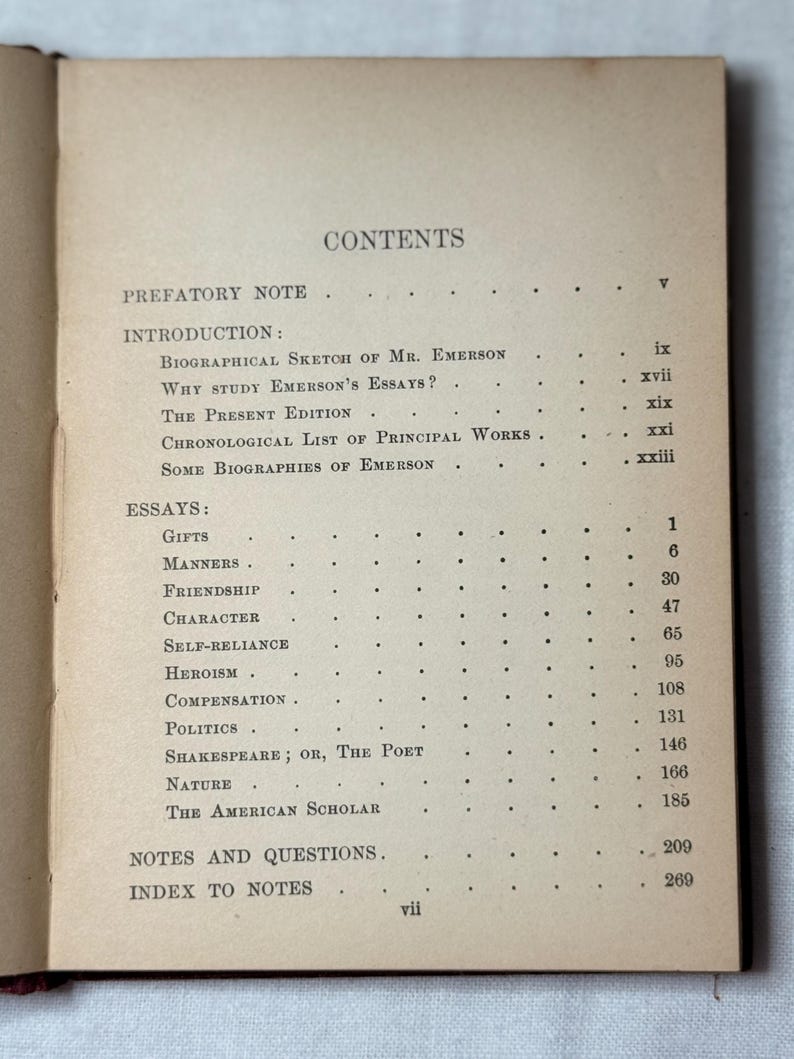 May include: An open book showing a contents page with a list of essays. The paper has a tan colour, with titles such as "Gifts", "Manners", and "The American Scholar" listed. The book is open to page vii.