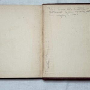May include: An open book with aged, off-white pages. The right page has handwritten text: "The Scarlet Letter, Autograph of the breakfast to W. reply 1910." A signature is visible on the left page. The book's cover is dark brown.