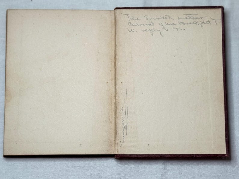 May include: An open book with aged, off-white pages. The right page has handwritten text: "The Scarlet Letter, Autograph of the breakfast to W. reply 1910." A signature is visible on the left page. The book's cover is dark brown.