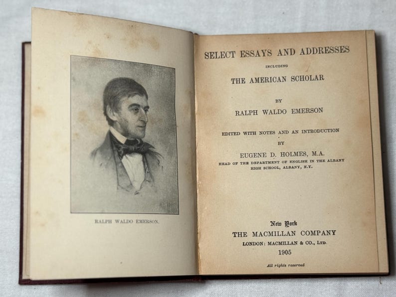 May include: An open book titled "Select Essays and Addresses" by Ralph Waldo Emerson. The left page displays a portrait of Emerson. Published in 1905 by The Macmillan Company, New York.