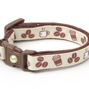 Peut inclure: Un collier de chat beige avec un ruban marron et une clochette. Le ruban a un motif répété de tasses à café et de grains de café.