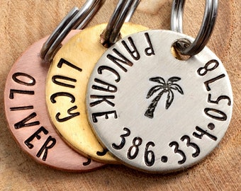 May include: Three round metal dog tags with engraved names and phone numbers. The tags are attached to key rings. The tags are copper, gold, and silver.