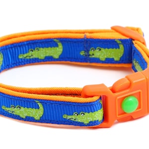 May include: Orange and blue cat collar with a green alligator print and a small bell.