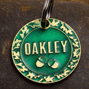 May include: Green metal dog tag with a gold border and acorn design. The tag says "OAKLEY" in gold lettering.