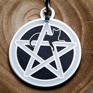 May include: A silver-toned pendant featuring a black cat silhouette inside a white pentagram on a dark blue background.