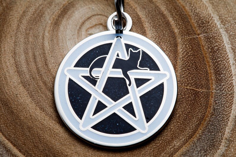 May include: A silver-toned pendant featuring a black cat silhouette inside a white pentagram on a dark blue background.