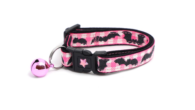 Puede incluir: Collar de gato de cuadros rosa y blanco con estampado de murci&eacute;lagos negros y una campanilla rosa.