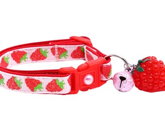May include: A red and white cat collar with a strawberry print and a red strawberry charm with a bell.