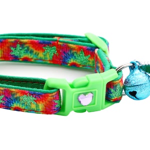 May include: A green and rainbow tie-dye cat collar with a green leaf charm and a blue bell.