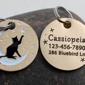 May include: Gold-toned pet ID tag with a black cat silhouette on a crescent moon with stars. The back side of the tag has the name "Cassiopeia", phone number "123-456-7890", and address "286 Bluebird Ln."