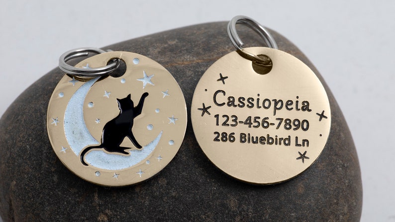 May include: Gold-toned pet ID tag with a black cat silhouette on a crescent moon with stars. The back side of the tag has the name "Cassiopeia", phone number "123-456-7890", and address "286 Bluebird Ln."