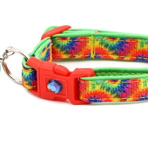 May include: A green and tie-dye patterned dog collar with a red buckle and a peace sign charm.