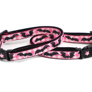 Puede incluir: Dos collares para gatos rosa y negro con un patr&oacute;n de murci&eacute;lago. Un collar tiene una campana rosa y el otro tiene un amuleto de murci&eacute;lago negro.